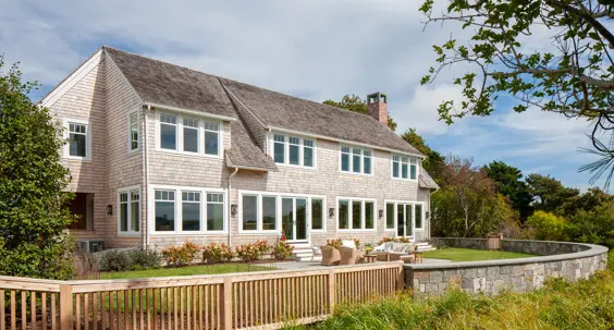 The rear exterior of this shingle-style home with many windows to take advantage of its waterfront location.