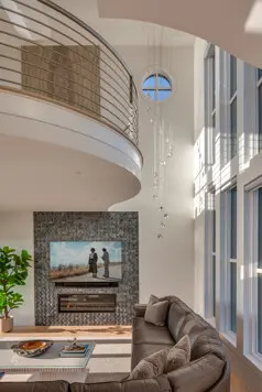 Double-height living spaces are softened by a curved rail, sculptural ceiling, and cascading pendant that draws the eye between levels.