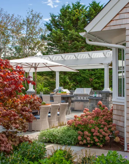 A new patio, outdoor kitchen, pergola, and firepit create seamless indoor-outdoor living while preserving open yard space for gathering and play.